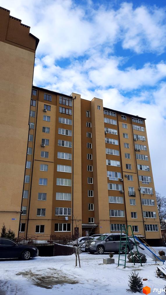 Будинок на вул. Чорновола, 128а, має світло-бежевий фасад та багато вікон. Біля будинку розташовані автомобілі та дитячий майданчик.
