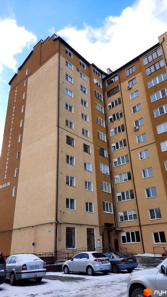 Фасад житлового комплексу на вул. Чорновола, 128а, з вікнами та кондиціонерами. Прибудинкова територія засніжена, з припаркованими автомобілями.