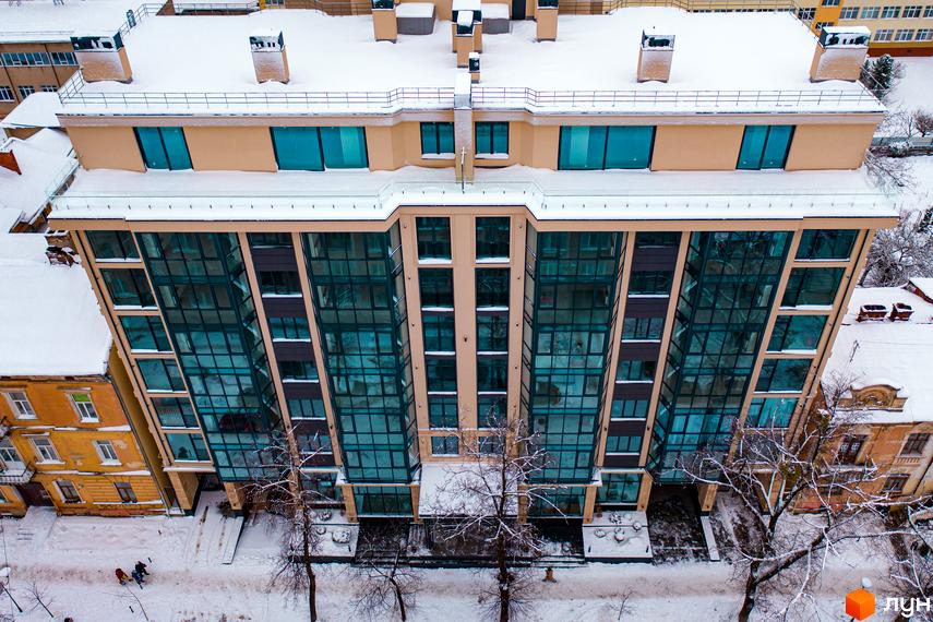 Зовнішній вигляд житлового комплексу Royal Hall з панорамним склінням та снігом на даху. Навколо будинку дерева та засніжена територія.