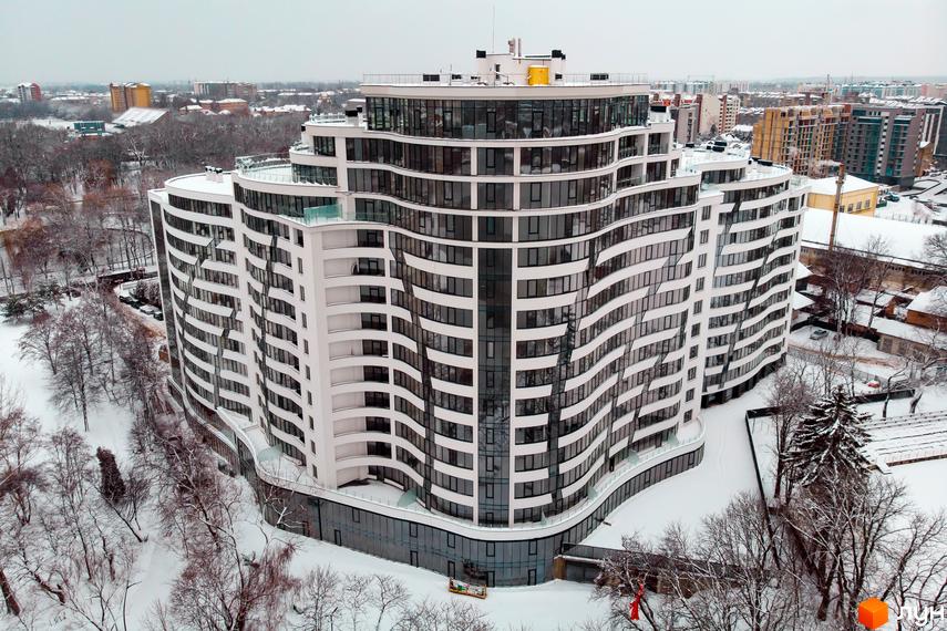 Зображення багатоповерхового будинку з великими вікнами. Навколо Житлового комплексу Parus дерева в снігу.