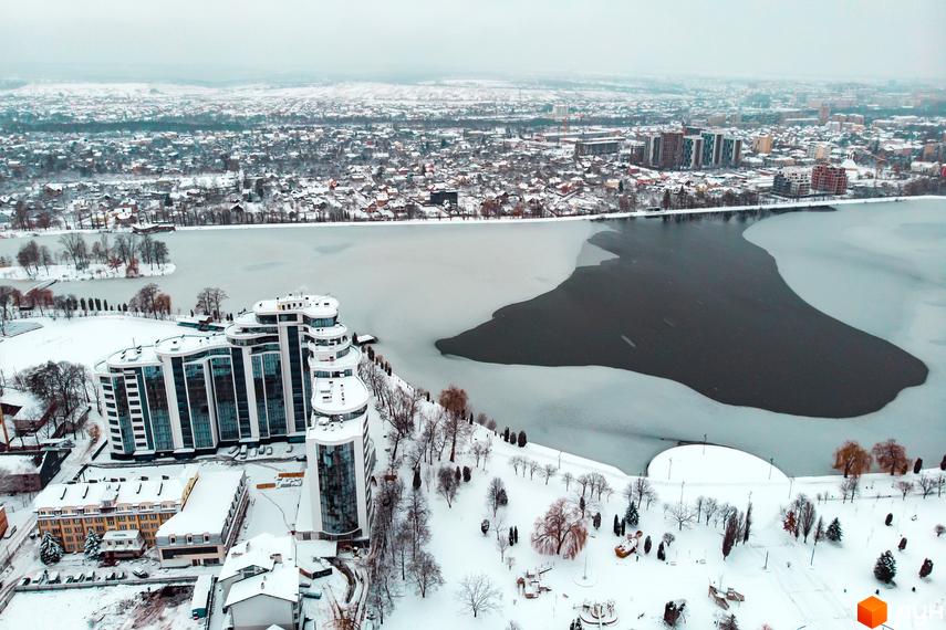 Зимовий вид на Житловий комплекс Parus з висоти пташиного польоту. Будівлі з великими вікнами, засніжена прибудинкова територія та частково замерзле озеро.