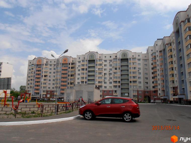 Зовнішній вигляд житлового комплексу Юність з парковкою та прибудинковою територією, де розташовані дитячі майданчики.