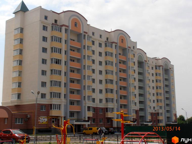 Житловий комплекс Юність з фасадом у світлих тонах та балконами. Прибудинкова територія з дитячим майданчиком та парковкою.