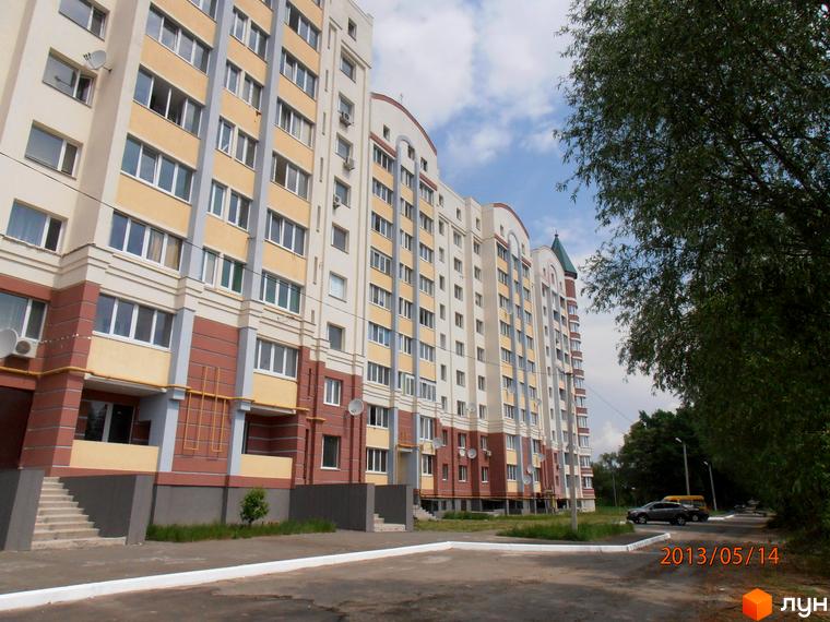 Житловий комплекс Юність з фасадом, що складається з жовтих і коричневих панелей. Прибудинкова територія з зеленими насадженнями та автомобілями.