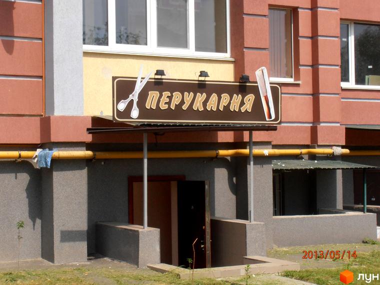 Зовнішній вигляд будинку житлового комплексу Юність з вивіскою перукарні та прибудинковою територією.