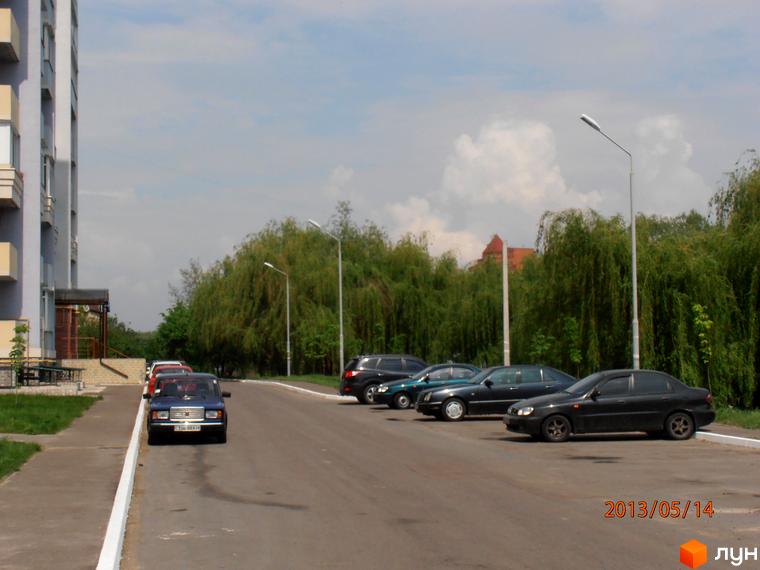 Зовнішній вигляд житлового комплексу Юність з парковкою та зеленими насадженнями на прибудинковій території.
