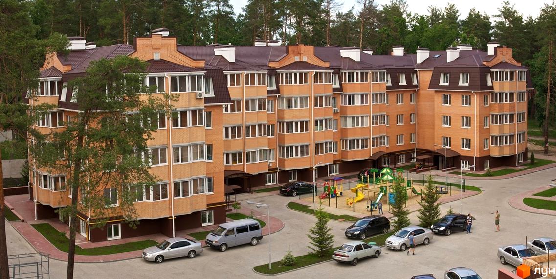 Житловий комплекс Суворов з багатоповерховими цегляними будинками та коричневим дахом, прибудинкова територія з дитячим майданчиком та парковкою.