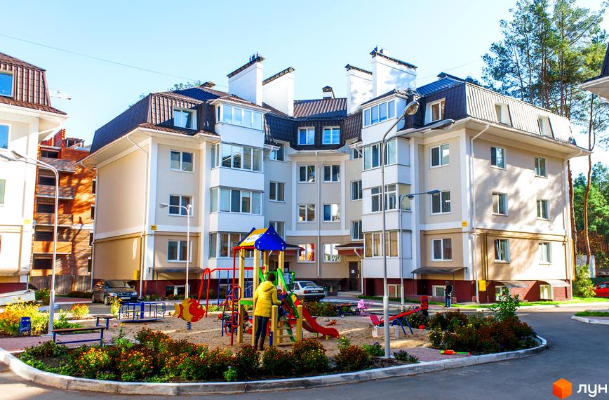 Багатоквартирні будинки Житлового комплексу Матросова з бежевими фасадами та темними дахами. На передньому плані дитячий майданчик з пісочницею та квітучими клумбами.