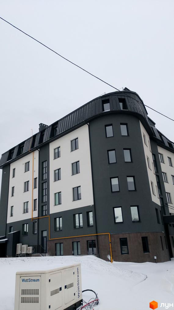 Зовнішній вигляд новобудови на вул. Довга, 56, 56а, з сірими та білими фасадами та темним дахом. На прибудинковій території видно генератор та сніг.