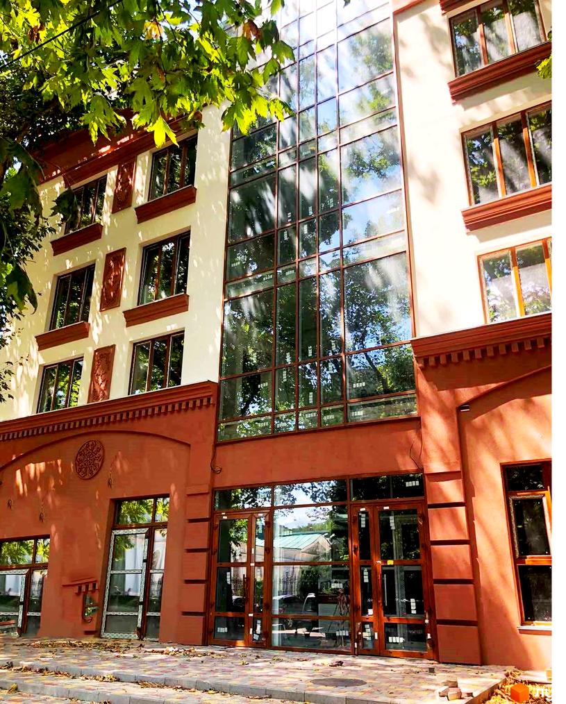 Фасад будівлі ЖК L7 House з великими вікнами, що відбивають дерева. Перед будинком тротуар з плиткою та зелені насадження.