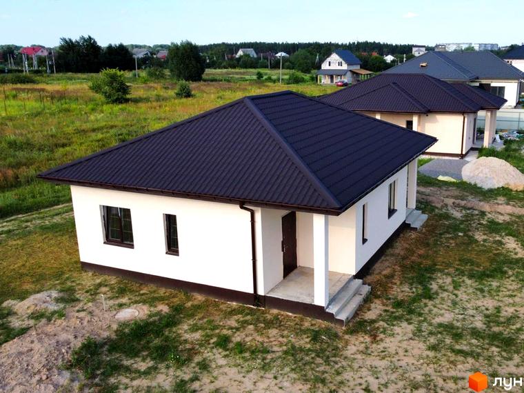 Котеджне містечко КМ Лісовий Масив: білий одноповерховий будинок з темно-коричневим дахом та прибудинковою територією.