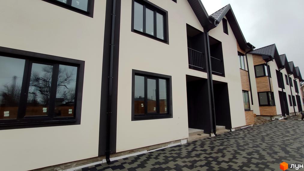 Зовнішній вигляд новобудови КМ Admiral Park Debut з сірими вікнами та дверима, чорними водостічними трубами та сірою бруківкою. На прибудинковій території видно дерева.