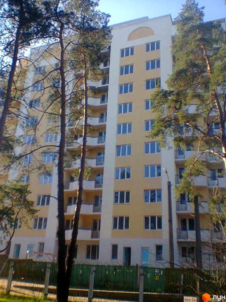 Багатоповерховий житловий будинок на вул. Полтавська, 69, світло-жовтого кольору з білими балконами. Перед ним високі сосни та зелений паркан.