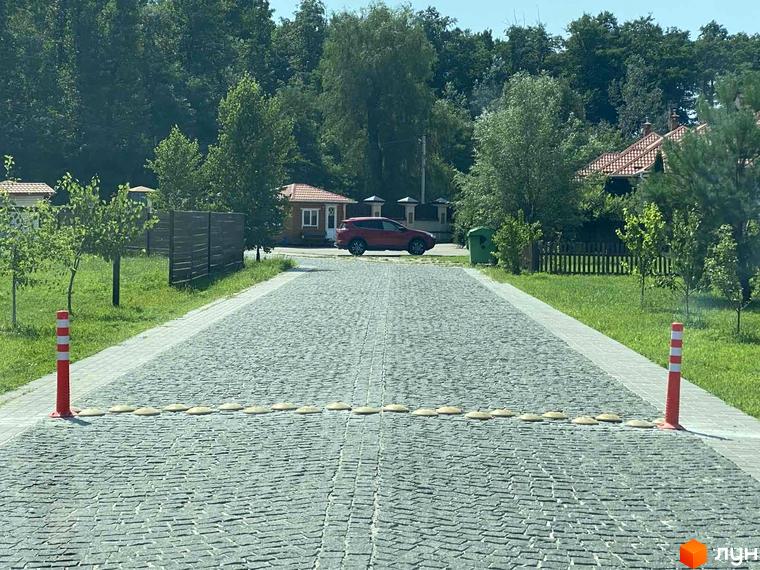 Котеджі з червоними дахами Котеджного містечка Щасливе Життя розташовані серед зелені. До них веде брукована дорога.