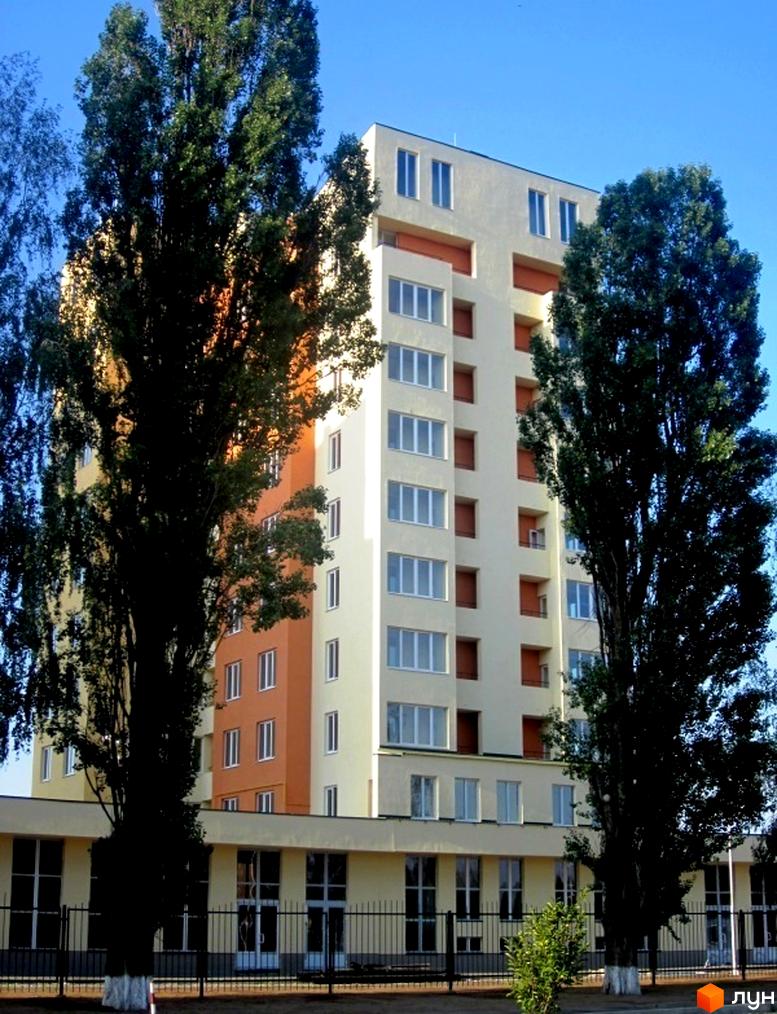 Житловий комплекс Новосельцево з фасадом у світлих тонах та великими вікнами. Прибудинкова територія озеленена деревами.