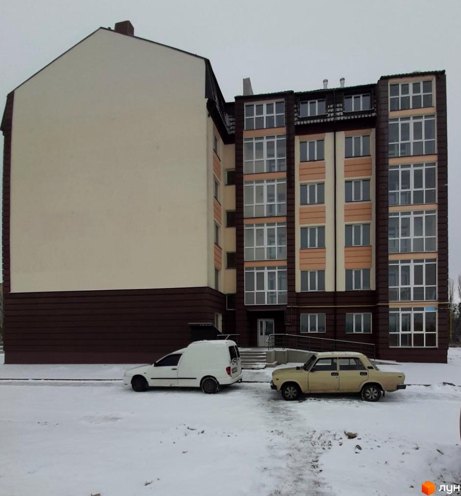 Зовнішній вигляд житлового комплексу Тульчинський посад з білою та бежевою обробкою фасаду, темним дахом та коричневим цоколем. На прибудинковій території видно дві машини та засніжену місцевість.