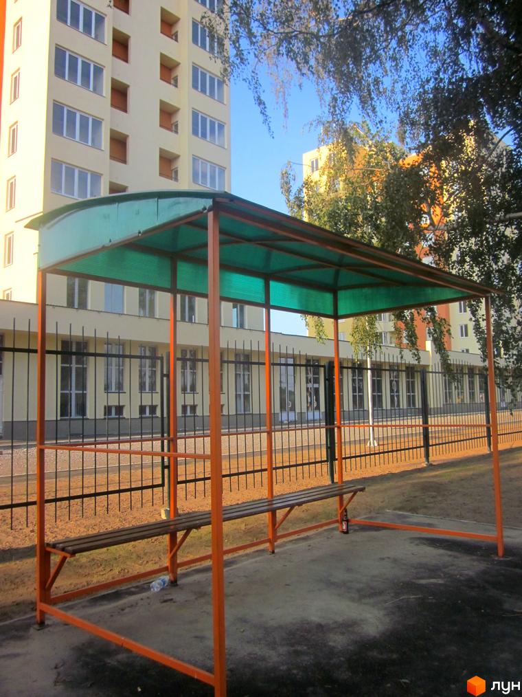 Зовнішній вигляд будинку ЖК Новосельцево. На прибудинковій території розташований навіс для очікування транспорту з лавкою.