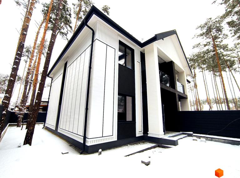 Білий двоповерховий будинок з чорними акцентами на фасаді серед засніжених дерев. Перед будинком сніг, що підкреслює архітектуру.