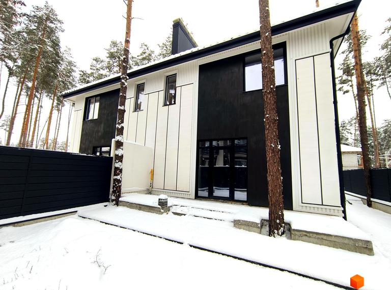 Зовнішній вигляд будинку дуплексів Toscana Home взимку, з чорно-білим фасадом та новорічною ялинкою на прибудинковій території.