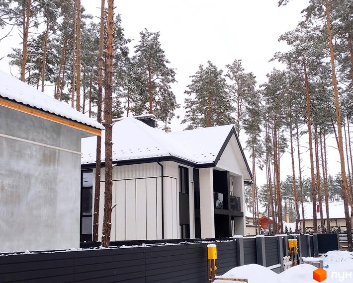Дуплекси Toscana Home - це двоповерхові будинки з біло-чорним фасадом та снігом на даху, розташовані серед високих сосен. На території видно паркан та елементи благоустрою.