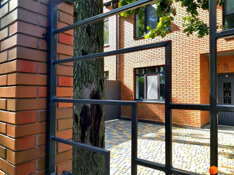 Фасад таунхауса BRIGHTON GARDEN з цегли та вікнами з чорними рамами. Перед будинком викладена бруківка та видно частину огорожі.