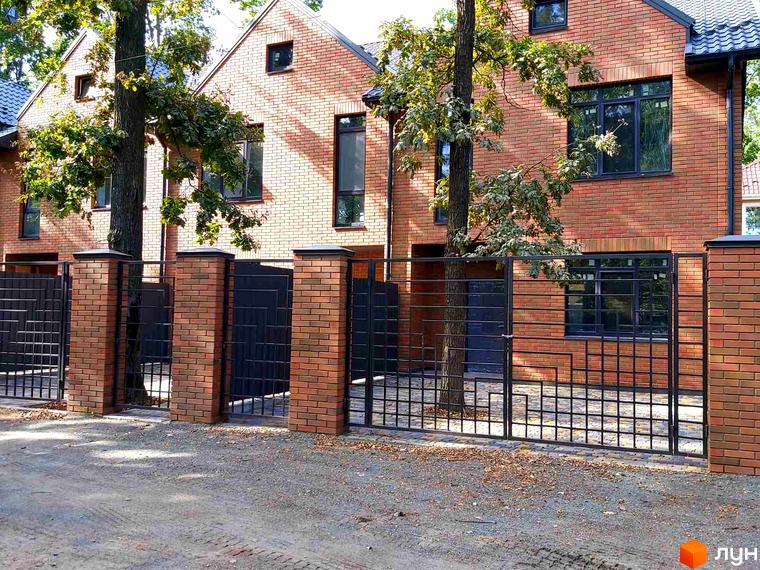 Таунхауси BRIGHTON GARDEN: цегляні будинки з темними вікнами та дахами. Перед будинками розташована чорна металева огорожа з цегляними стовпами.