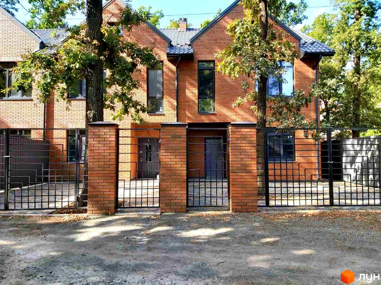 Таунхауси BRIGHTON GARDEN з червоної цегли з чорним парканом та зеленими деревами.