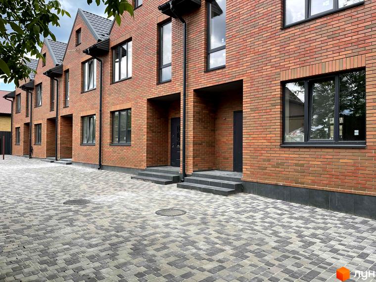 Таунхауси BRIGHTON GARDEN з червоної цегли з великими вікнами та сірим дахом. Перед будинками вимощена сіра бруківка.