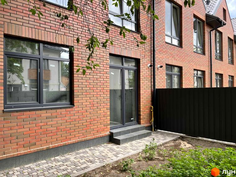 Фасад таунхаусів BRIGHTON GARDEN з червоної цегли, великими вікнами та темними рамами. Поруч вимощена доріжка та зелені насадження.