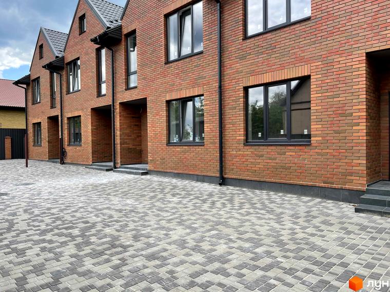 Зовнішній вигляд таунхаусів ELEGANT з червоної цегли з темними вікнами. Перед будинками вимощена сіра бруківка.