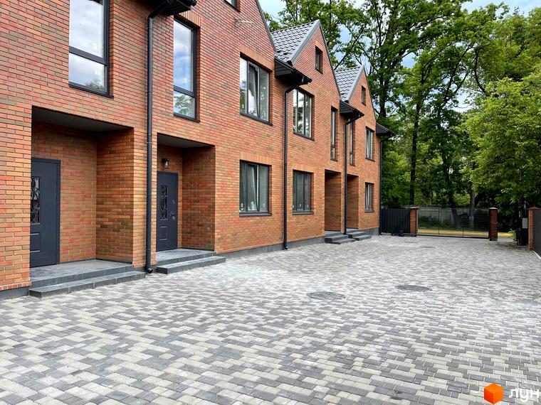 Таунхауси ELEGANT з червоної цегли з сірим дахом та бруківкою перед будинком. На території комплексу є паркан та зелені насадження.