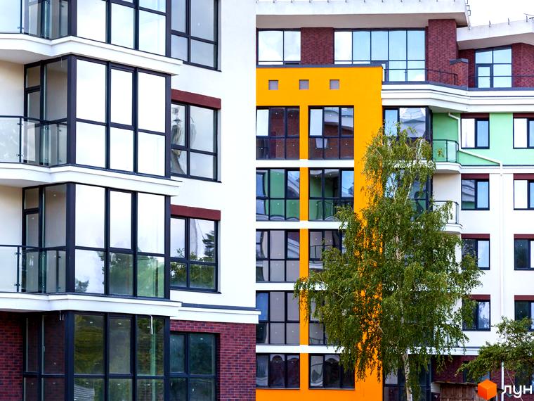 Новобудова ЖК Лісова казка 2 з яскравим фасадом та великими вікнами. Зелені насадження біля будинку.