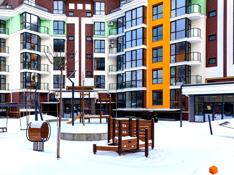 Житловий комплекс Лісова казка 2: багатоповерховий будинок з яскравими фасадами та дитячим майданчиком взимку. Зовнішній вигляд новобудови та прибудинкової території.