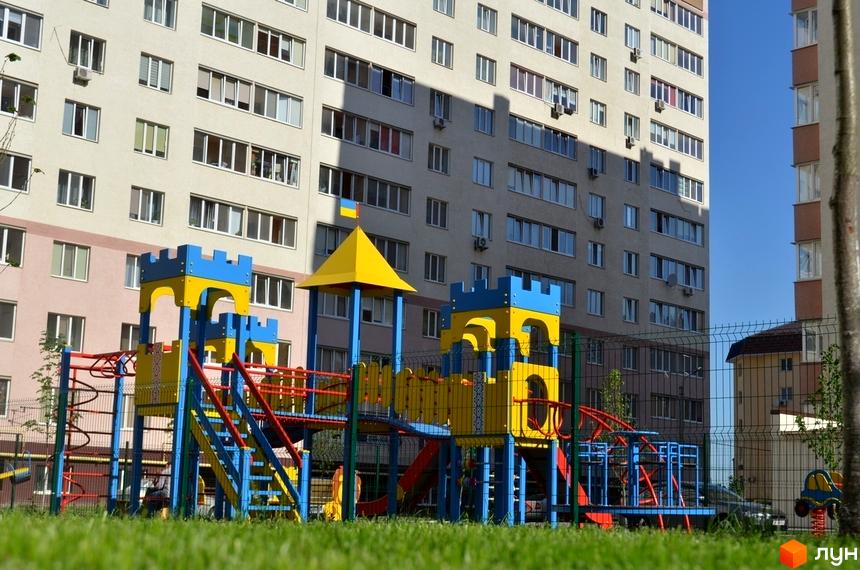 Житловий комплекс Софіївська Слобідка: багатоповерховий будинок з численними вікнами та дитячим майданчиком біля нього. Територія комплексу доглянута, з зеленою травою.