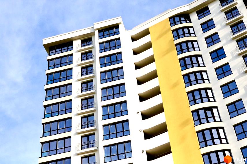 Фасад житлового комплексу Lystopad з великою кількістю вікон та балконів. Будівля має білий колір та жовту вставку, що надає їй виразності.