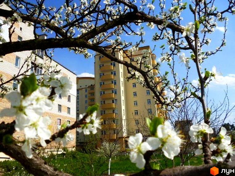 Житловий комплекс ЖК Яблуневий з квітучими деревами на прибудинковій території та сучасною архітектурою будинку.