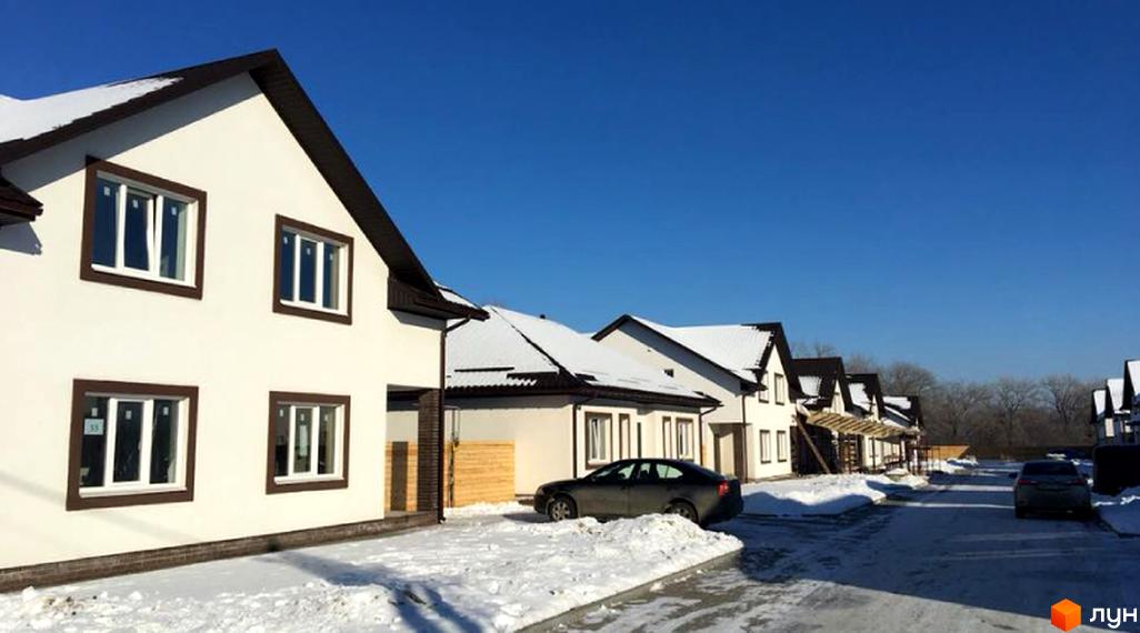 Котеджне містечко КМ Титул. Білі двоповерхові будинки з коричневими дахами та вікнами, вкриті снігом, розташовані на засніженій вулиці.