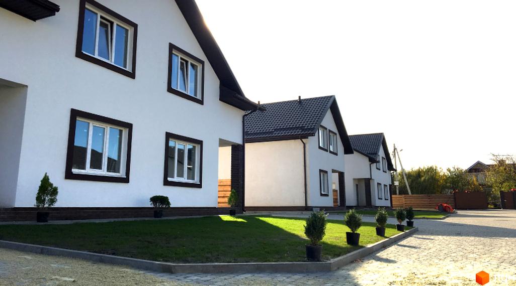 Котеджне містечко КМ Титул: білі будинки з темними дахами та вікнами, доглянута прибудинкова територія з газоном та зеленими насадженнями.