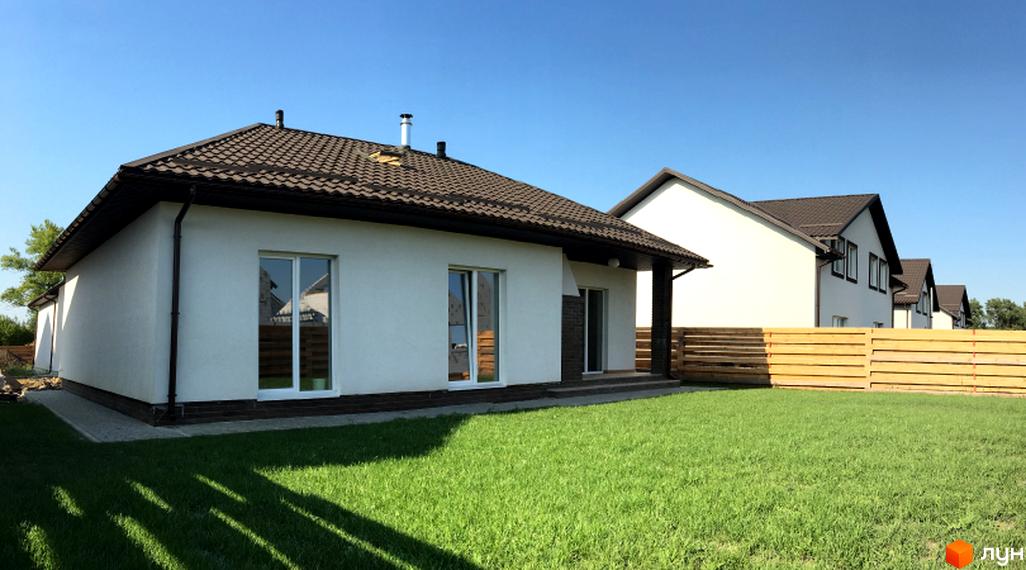 Котеджне містечко КМ Титул: білі будинки з коричневими дахами та зелений газон. На території розташована дерев'яна огорожа та доглянутий двір.