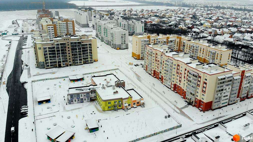 Зовнішній вигляд житлового комплексу Мікрорайон „Академічний“ взимку. Багатоповерхові будинки з жовтими та білими фасадами, дитячий садок та прибудинкова територія, вкрита снігом.