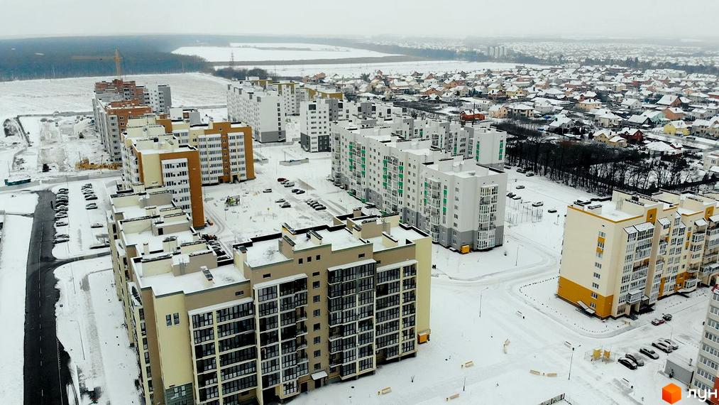 Мікрорайон „Академічний“: сучасний житловий комплекс із багатоповерховими будинками, розташований на тлі зимового пейзажу з полями та лісом. Прибудинкова територія вкрита снігом, видно дороги та припарковані автомобілі.