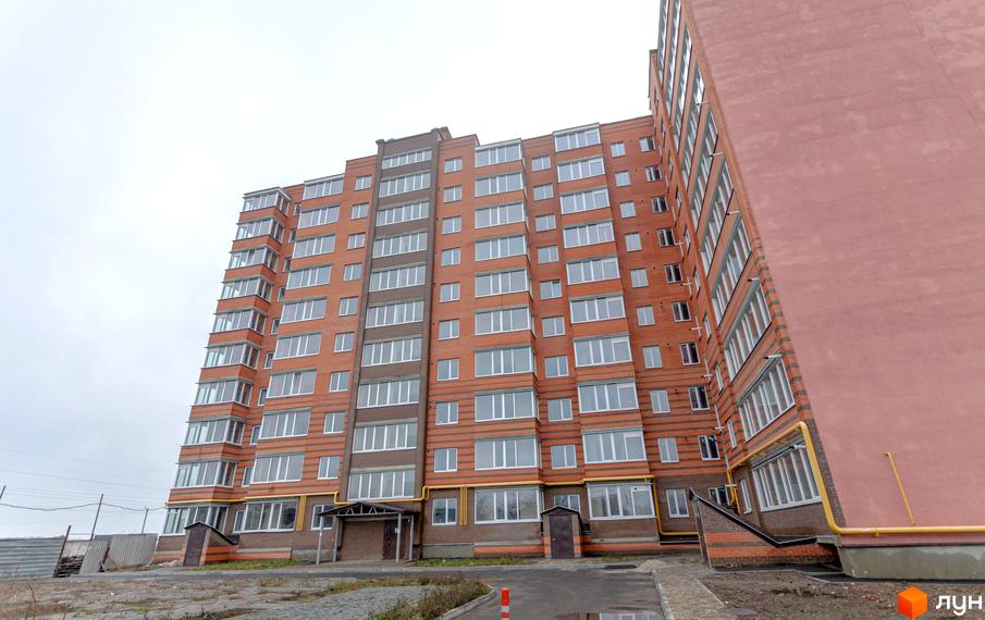 Зовнішній вигляд цегляної новобудови ЖК Петрівський Квартал з численними вікнами та балконами. Навколо будинку облаштована прибудинкова територія з доріжками та зеленими насадженнями.