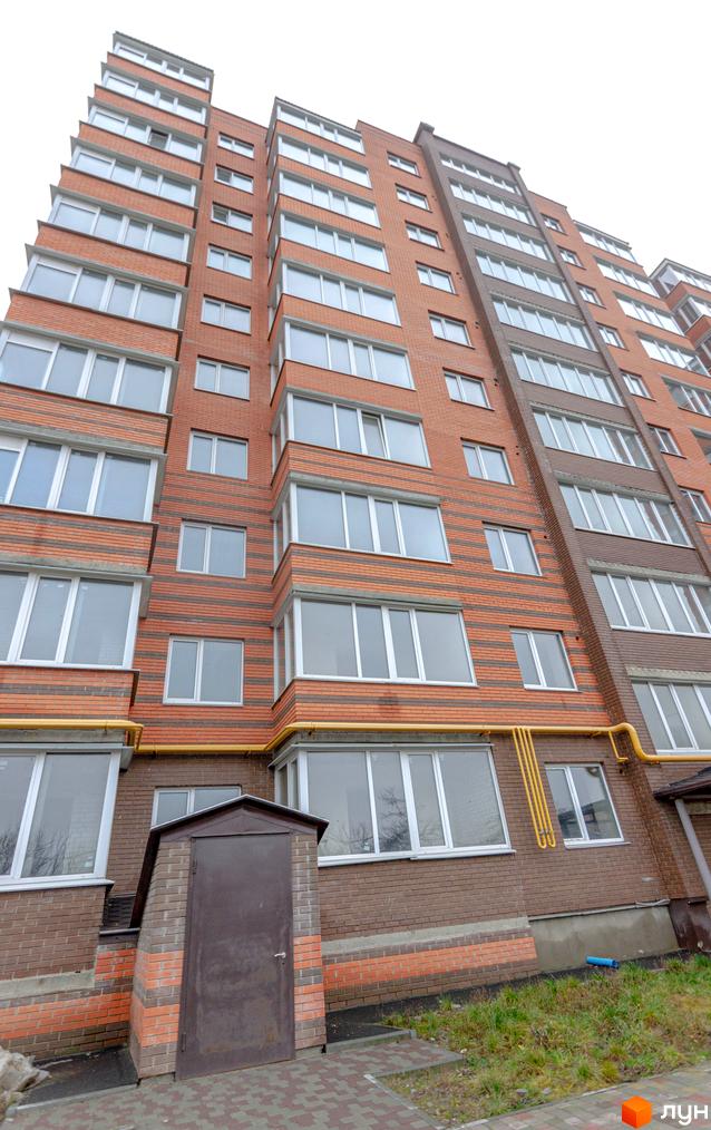 Зовнішній вигляд багатоквартирного будинку ЖК Петрівський Квартал з цегляним фасадом та великими вікнами. Прибудинкова територія з доріжками та зеленню.