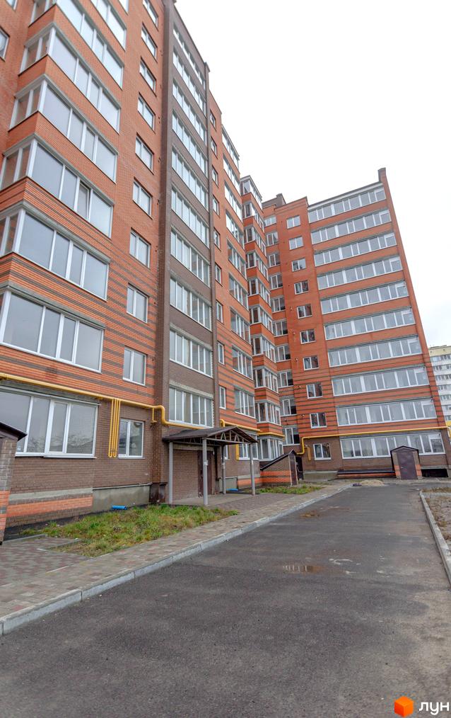 Зовнішній вигляд новобудови ЖК Петрівський Квартал з цегляним фасадом та великою кількістю вікон. Прибудинкова територія з асфальтованою дорогою та тротуаром.