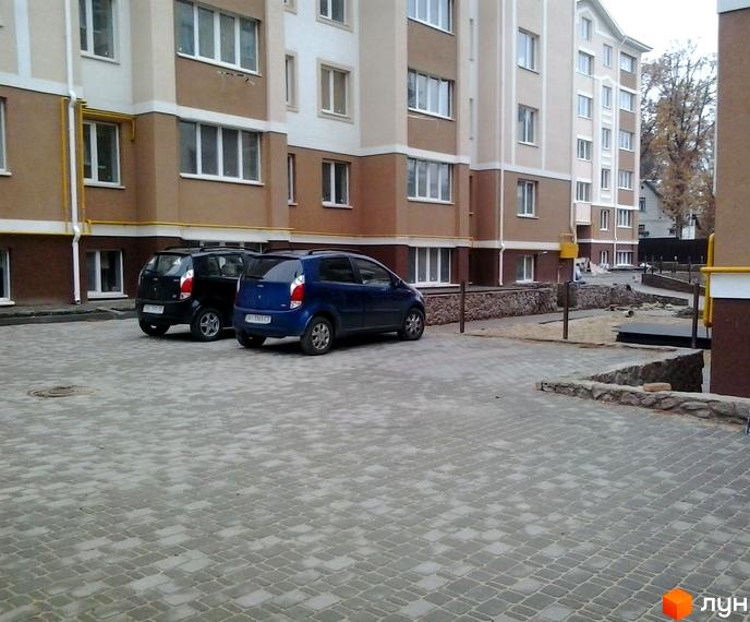 Житловий комплекс Квартал на „Київській“ з двома автомобілями на прибудинковій території та сучасним фасадом будинку.