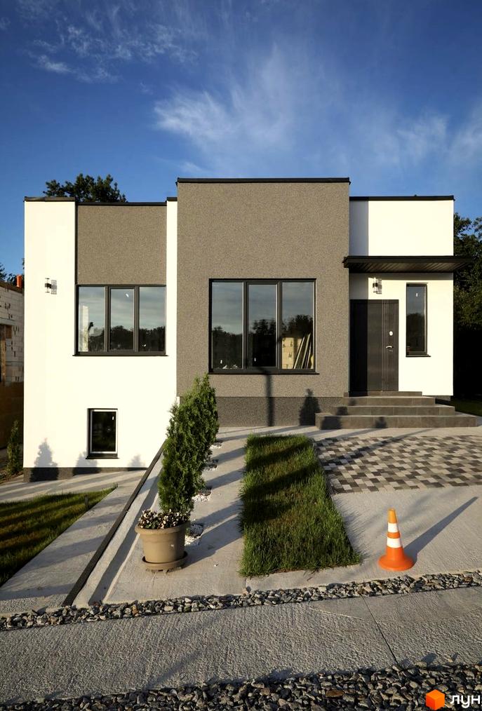 Котеджне містечко КМ Терещенські Озера: двоповерховий будинок з білою та сірою штукатуркою, великими вікнами та вхідною групою. На прибудинковій території – доглянутий газон, зелені насадження та бруківка.