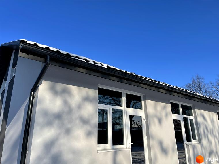 Зовнішній вигляд таунхаусів Oak-Park з білою штукатуркою та чорними вікнами на тлі блакитного неба та снігу. Комплекс розташований у мальовничому місці.