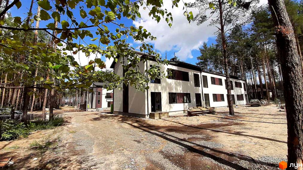 Білосніжний будинок з темними вікнами в Містечку котеджів Лісове-2. Навколо будівлі розташована прибудинкова територія з гравієм та деревами.