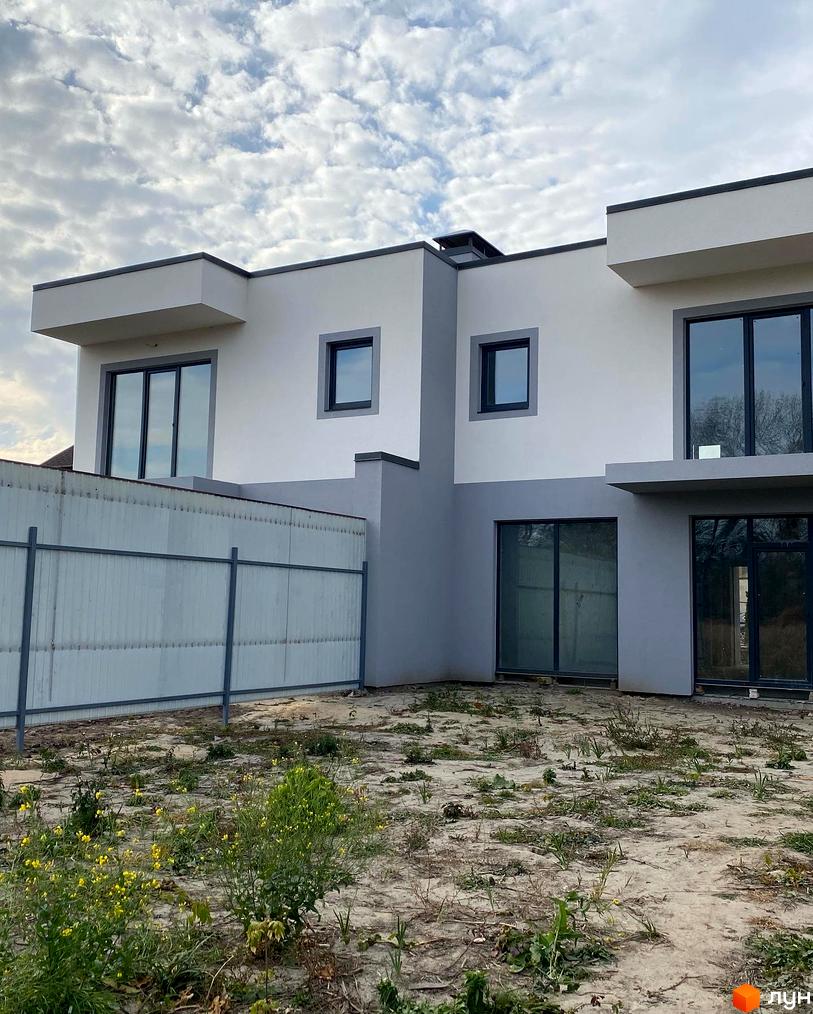 Зовнішній вигляд котеджного містечка Чапаєвка з сірими та білими фасадами, великими вікнами та прибудинковою територією з невисокою рослинністю.