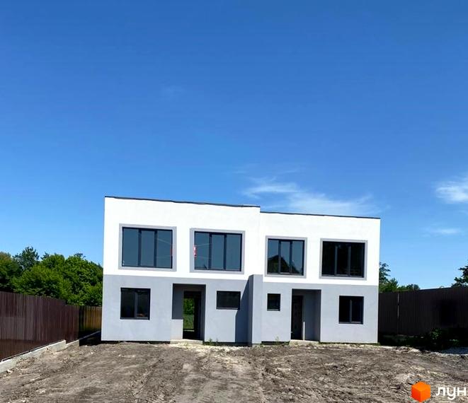 Котеджне містечко Чапаєвка: двоповерхові будинки з великими вікнами та сірим оздобленням фасаду на тлі блакитного неба. Територія навколо будинку вкрита ґрунтом.